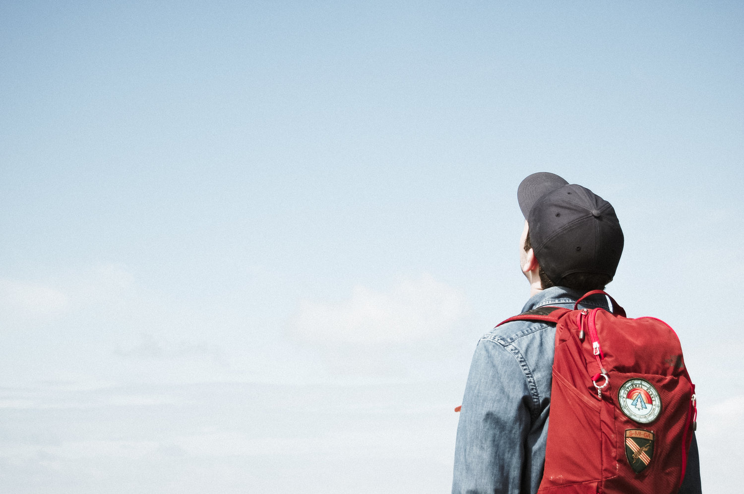 Teenager wearing backpack and hat facing towards the sky