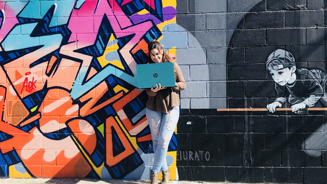 Yerelyn Nunez posed on her laptop in front a graffiti mural