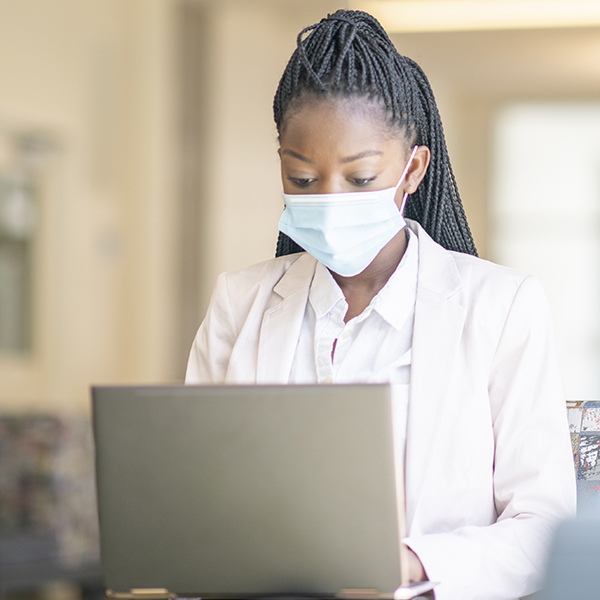 Female student typing on laptop while wearing mask