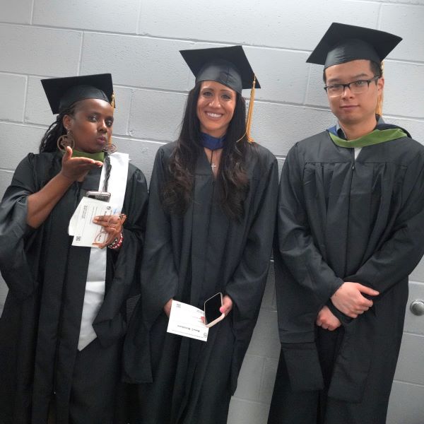 Three graduates of the first CUNY SPS MS HIM class smile and wave before the 2023 Commencement ceremony
