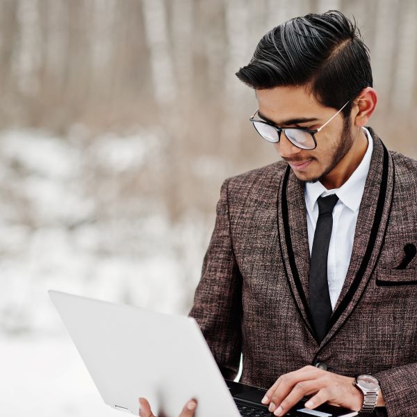 South Asian Male Student Wearing Blazer and Holding Laptop in Snowy Woods