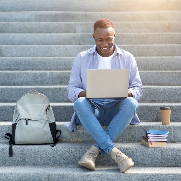 industrious-black-guy-studying-online-with-laptop-on-city-steps