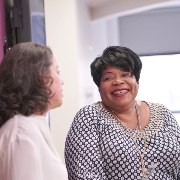 Two female CUNY SPS students smiling in campus hallway