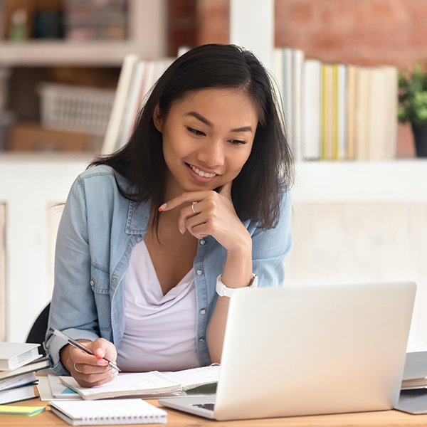 Smiling Asian undergraduate student studying in library with laptop