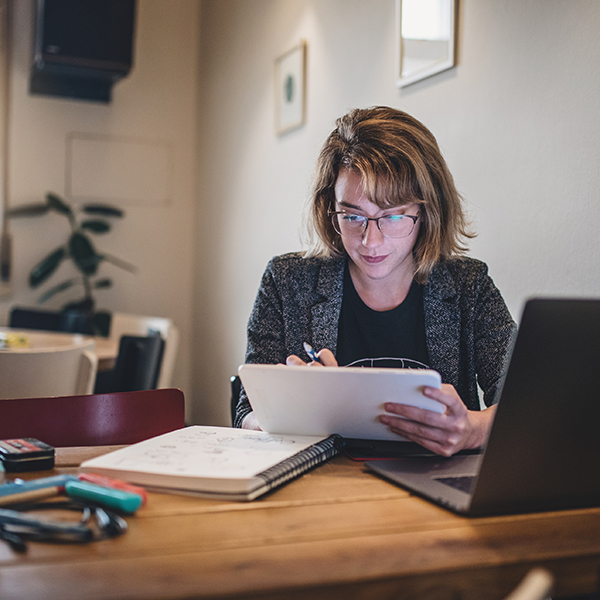 Woman in home office writing down notes in tablet