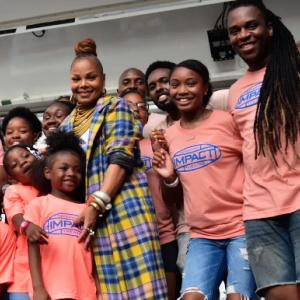 Group of young smiling black students in orange shirts surround a black man and black woman.