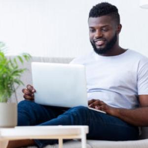 African American man sitting on the sofa studying on a laptop looking at the screen.