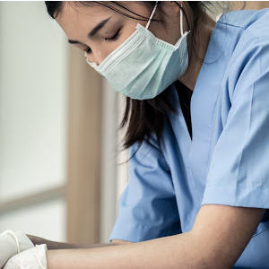 An Asian nursing wearing a mask sitting down taking a moment to herself