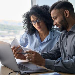 Adult male and female reviewing resumes sitting in front of a laptop