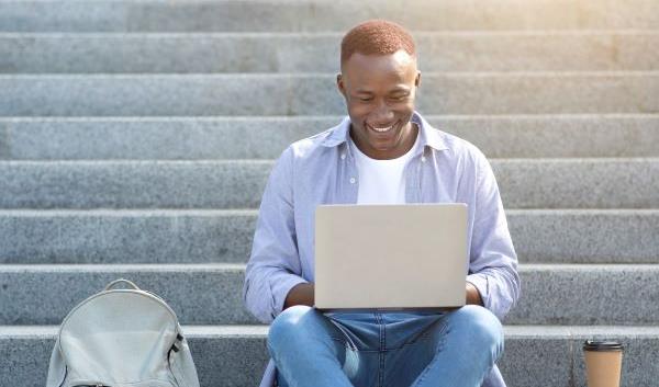industrious-black-guy-studying-online-with-laptop-on-city-steps