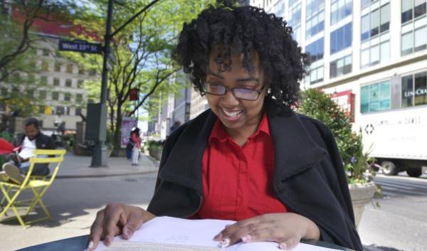 Student sitting at table in Manhattan's Herald Square Park looking at textbook in summer