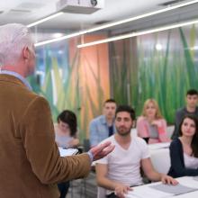 Male professor having a discussion with several male and female student in classroom