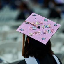 Image of female graduate at commencement wearing mortarboard that says "I Can Go the Distance"