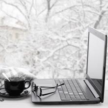 A photo of a laptop in front of a window looking out to snowy covered trees.