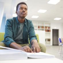 Portrait of young African-American man reading braille while studying in school library