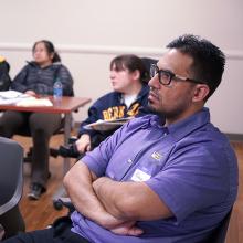 Male CUNY SPS student arms folded and seated during on campus event