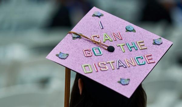 Image of female graduate at commencement wearing mortarboard that says "I Can Go the Distance"