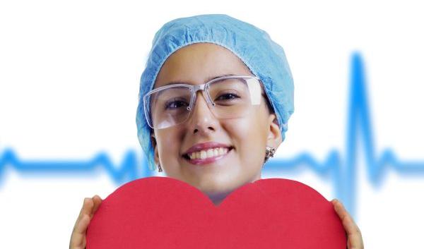 Photo of Female Nurse in Scrubs Smiling and Holding a Large Red Paper Heart